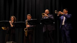 One woman and three men playing musical instruments on a stage.